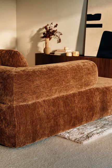Bruine zetel met afgeronde vormen in een warm interieur met donkere kast en decoratieve accenten.