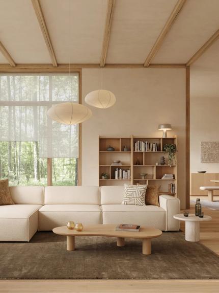 Canapé d’angle Isola beige dans un salon lumineux avec grandes fenêtres, bibliothèque en bois, table basse et matériaux naturels.
