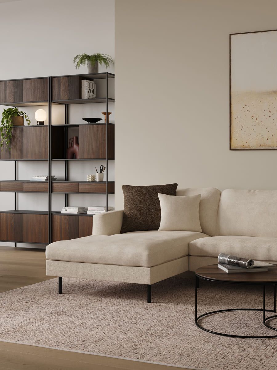 Een stijlvol en functioneel interieur voor een compacte ruimte, met een lichte, comfortabele bank, een strak houten boekenkast en minimalistische accessoires die warmte en balans toevoegen.