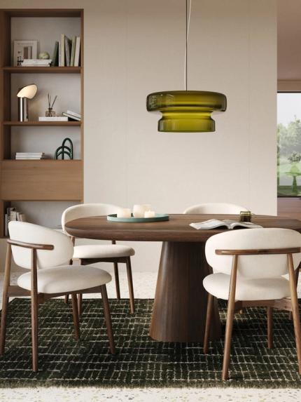 Gezellige eethoek met ronde houten tafel, lichte stoelen, groene hanglamp en houten kast, met doorkijk naar de woonkamer.