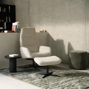Stijlvolle zithoek met beige fauteuil, voetenbank en een groot grijsgroen tapijt met structuurpatroon in een minimalistisch interieur.