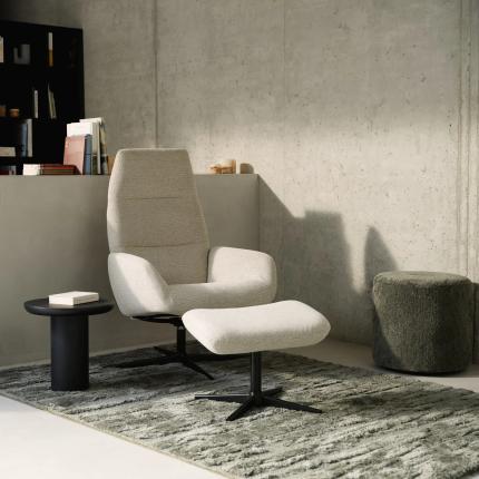 Stijlvolle zithoek met beige fauteuil, voetenbank en een groot grijsgroen tapijt met structuurpatroon in een minimalistisch interieur.