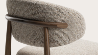 Detail van de Piola-stoel: gestoffeerde rug in grof weefsel met slanke armleuning in donker hout.