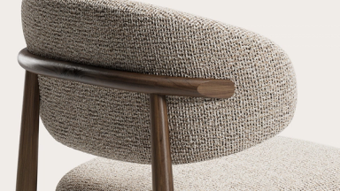 Detail van de Piola-stoel: gestoffeerde rug in grof weefsel met slanke armleuning in donker hout.