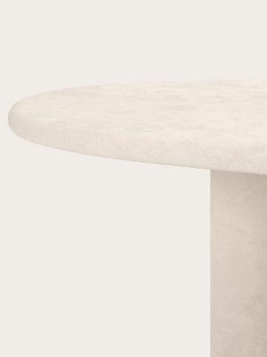 Close-up van een ronde tafel met een grof tafelblad met steenstructuur en een cilindervormig onderstel.