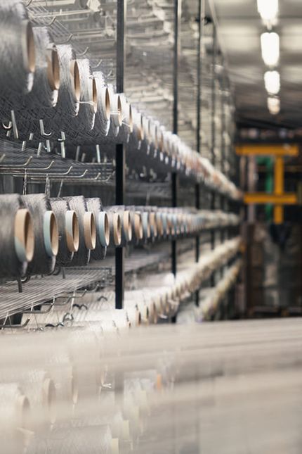 Rijen garens op spoelen in een textielproductieomgeving.
