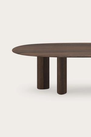 Langwerpige houten eettafel met afgerond blad en cilindervormige poten tegen een neutrale achtergrond.