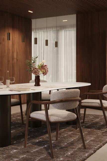 Gestoffeerde eetkamerstoelen rond een ovale tafel in een warm interieur met donker hout en open boekenkast.