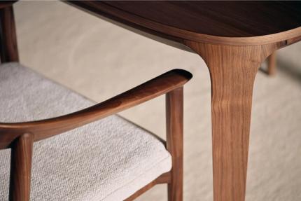 Close-up van de armleuning van een houten stoel, met een elegant design in walnoothout en een zacht gestoffeerde zitting.