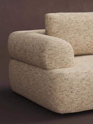 Close-up van een beige stoffen zetel met afgeronde armleuning en zachte, geweven bekleding tegen een donkerbruine achtergrond.