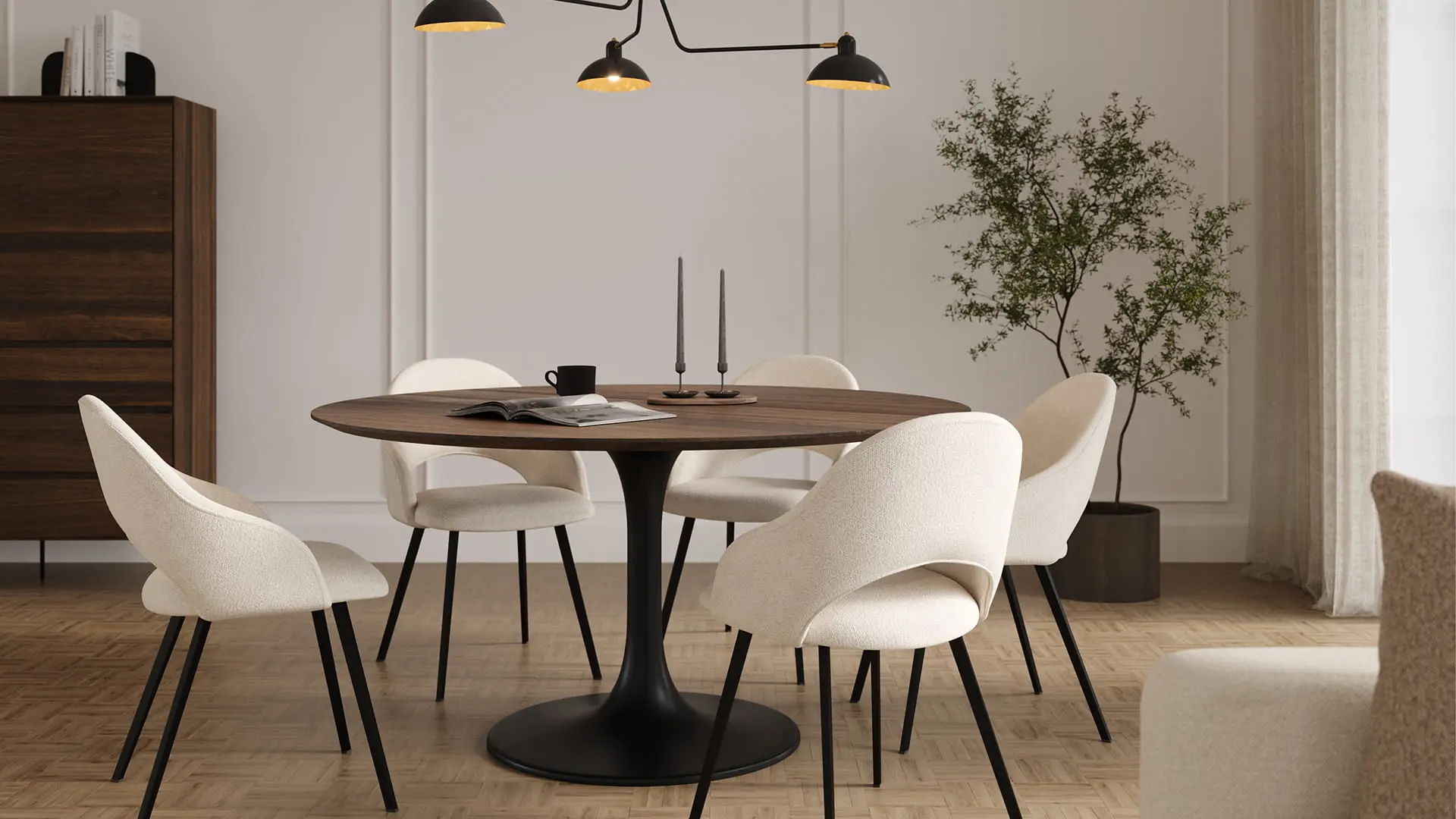Eetkamer met ronde houten tafel op zwart metalen voet, omringd door lichte stoelen met zwart metalen poten. Op tafel liggen kaarsen, een kopje en een open boek, met een groene plant op de achtergrond.