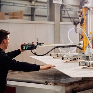 Vakman bedient machine tijdens productie van een tafelblad, met slangen en persarmen in een werkplaatsomgeving.