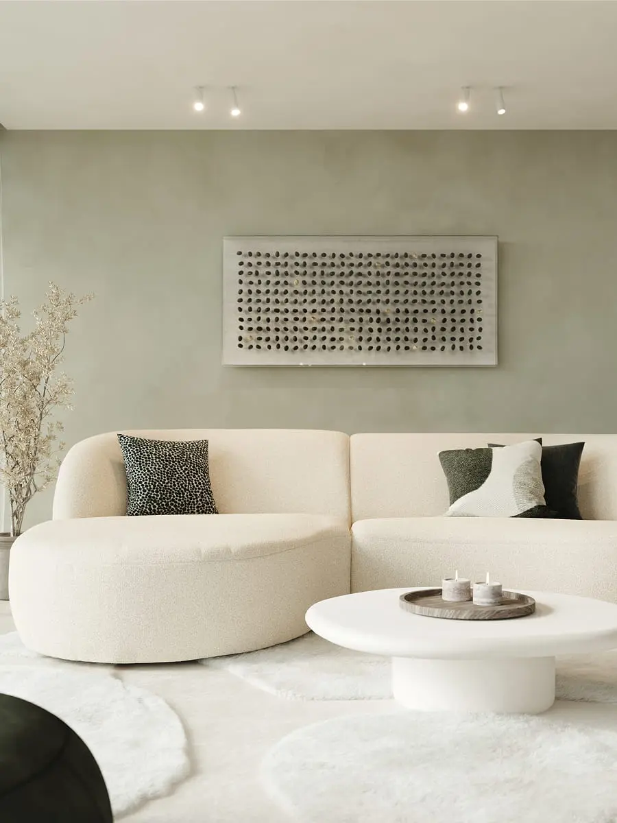 Beige zetel Tubo met afgeronde vormen in rustige woonkamer met ronde salontafel, zachte tapijten en groene wand.