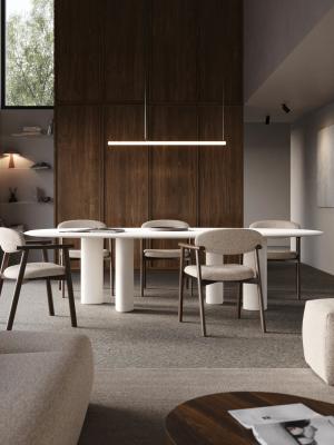 Moderne witte ovale eettafel met cilindervormige poten, omringd door beige eetkamerstoelen met donker houten frame.