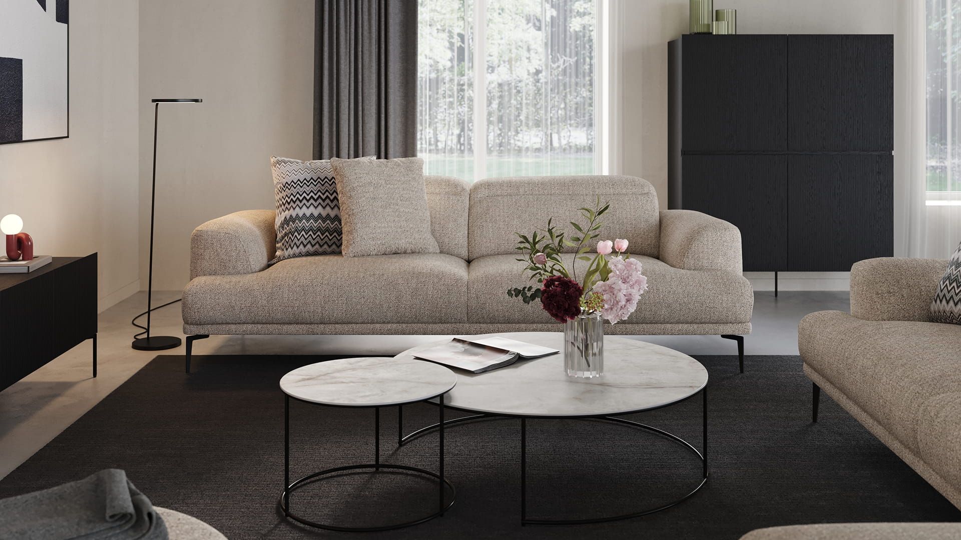 Grijze zetel Funchal in lichte woonkamer met ronde marmeren salontafels, zwarte kast, grote ramen en een vaas met bloemen.