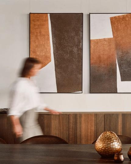Moderne eetkamer met abstracte kunst aan de muur, houten meubels en decoratieve objecten, met een persoon in beweging.
