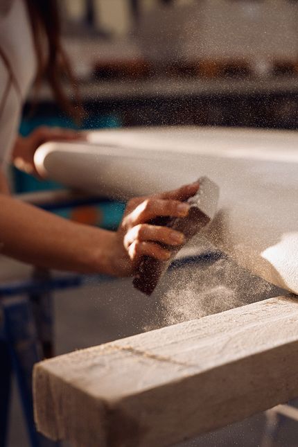 Artisan ponçant à la main un pied de meuble dans l'atelier, les particules de poussière illustrent le processus artisanal