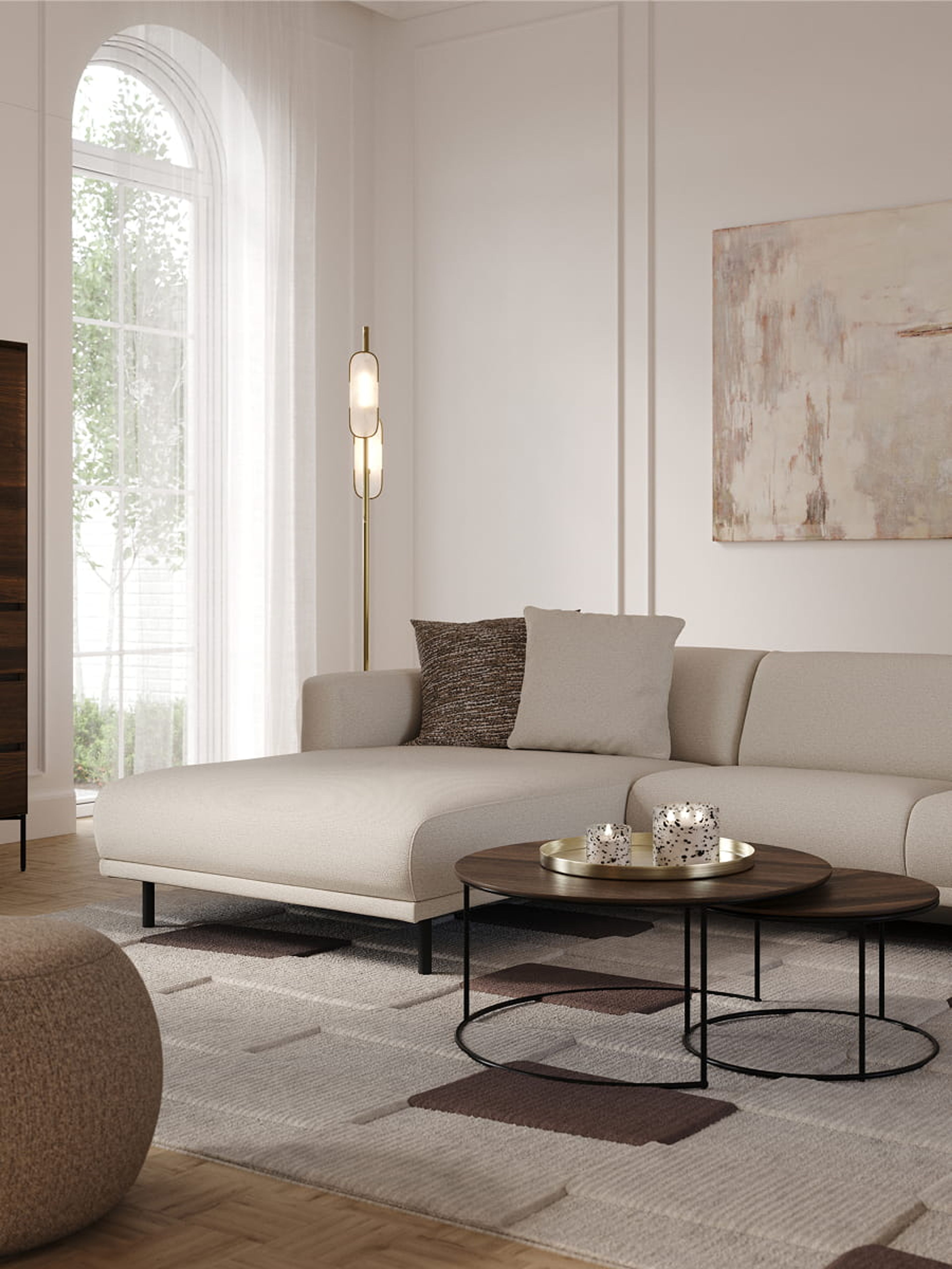 Canapé d’angle Evora beige clair avec méridienne dans un salon lumineux, avec tables basses rondes, lampadaire et tableau abstrait.