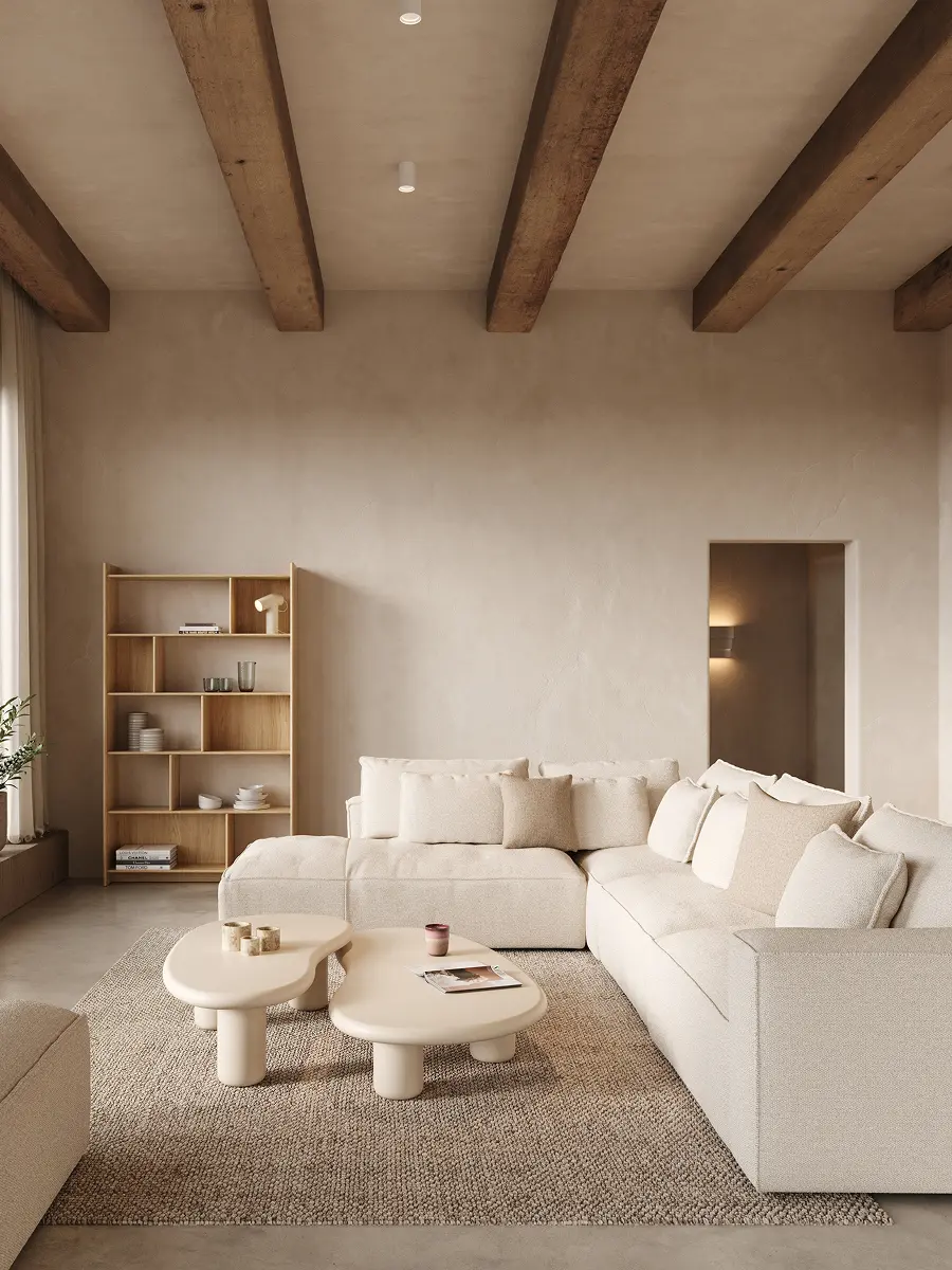 Canapé d’angle beige dans un salon apaisant avec poutres en bois, étagère ouverte et tables basses organiques sur tapis neutre.