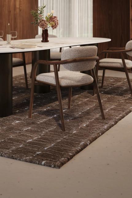 Gestoffeerde eetkamerstoelen rond een ovale tafel in een warm interieur met donker hout en open boekenkast.