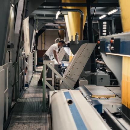 Medewerker bedient een industriële textielmachine in een tapijtfabriek waar garens machinaal worden verwerkt tot tapijten.