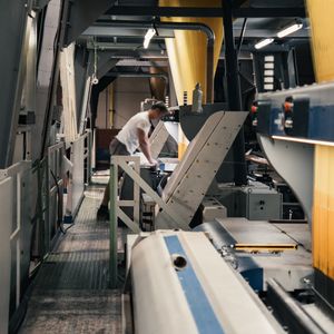 Un opérateur utilise une machine textile industrielle dans une usine de fabrication de tapis, où les fils sont transformés mécaniquement en tapis.