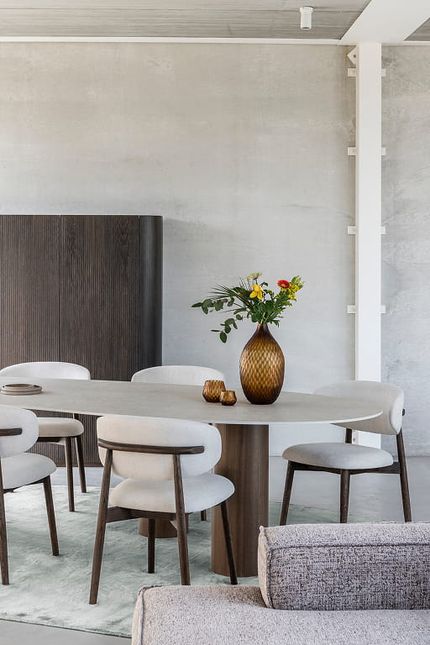 Lichte eetkamer met een ovale eettafel in houtlook, omringd door zes stoelen met donkerhouten poten en zacht gestoffeerde, lichtgekleurde zittingen en afgeronde rugleuningen.