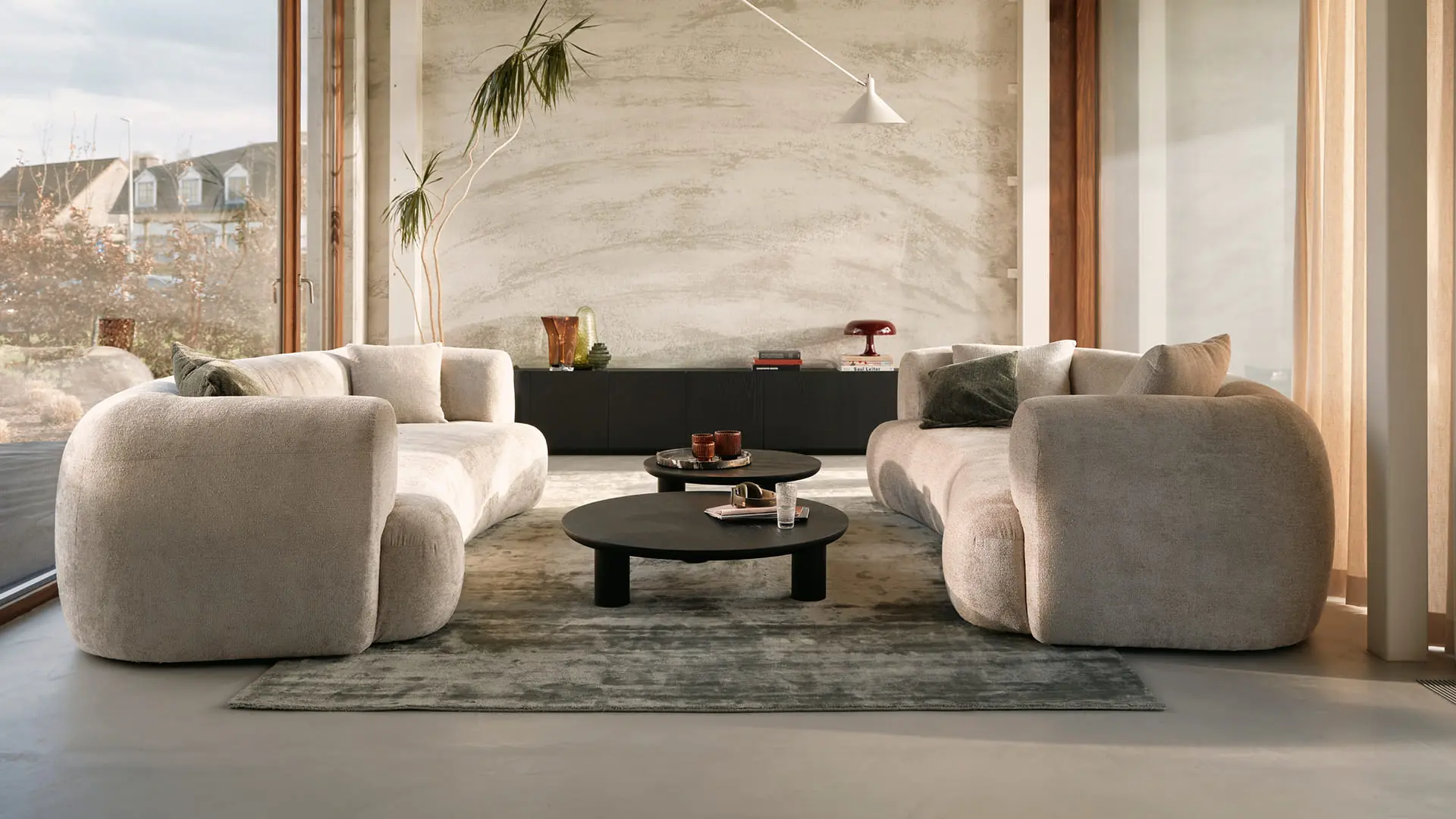 Moderne woonkamer met zachte, afgeronde zetel, ronde salontafels en minimalistisch interieur met veel natuurlijk licht