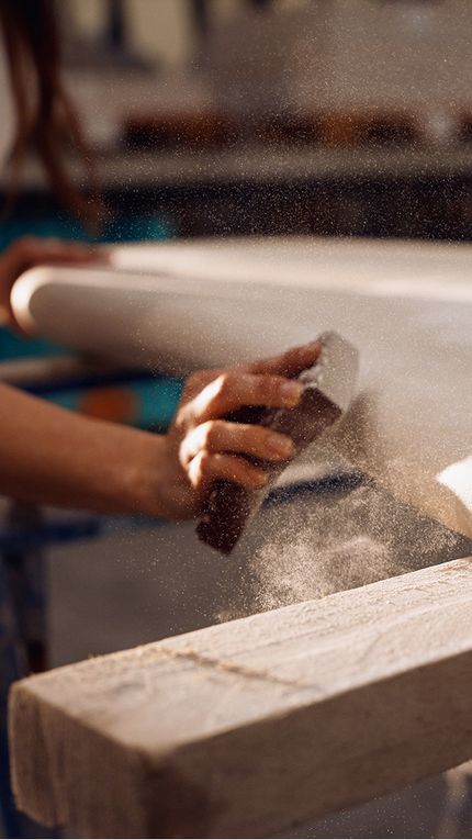 Vakman schuurt met de hand een meubelpoot af in het atelier, stofdeeltjes tonen het ambachtelijke proces