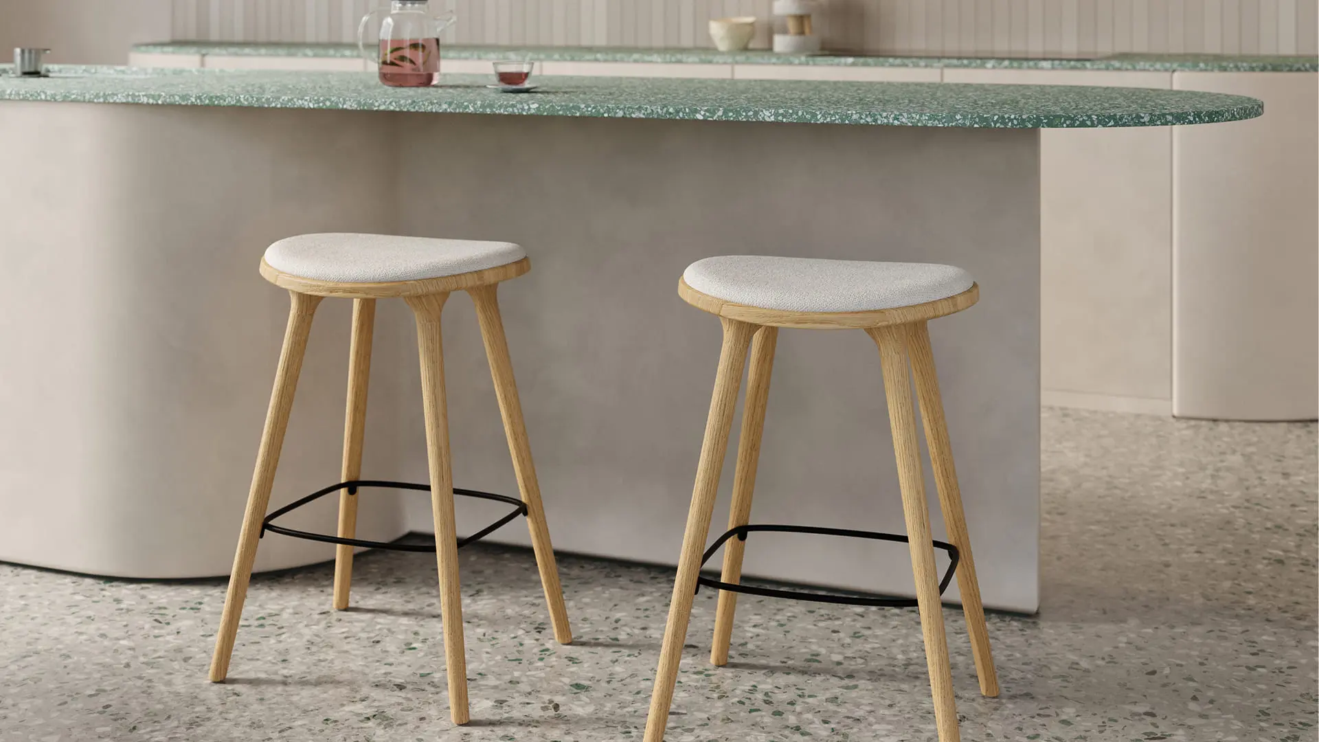 Twee houten barkrukken met licht gestoffeerde zitting onder een afgerond keukeneiland met groen gespikkeld blad, op een terrazzo vloer.