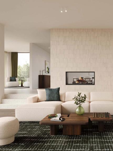 Beige hoekzetel Isola in lichte woonkamer met grote ramen, houten boekenkast, lage salontafel en zachte natuurlijke materialen.