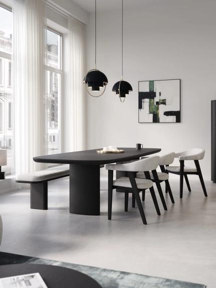 Minimalistische eetruimte met lange zwarte eettafel, lichte stoelen en bank, zwarte hanglampen en hoge ramen met transparante gordijnen.