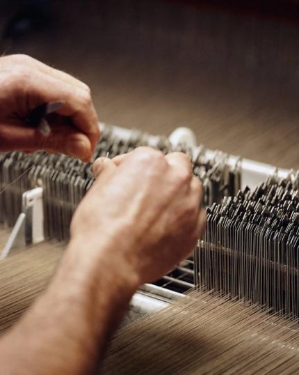 Des mains ajustent les fils sur un métier à tisser ; gros plan sur la production et les finitions textiles en atelier.