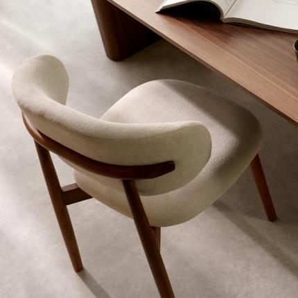 Close-up van een Piola stoel met beige bekleding en houten armleuningen, naast een houten tafel.