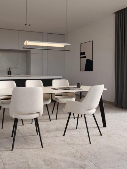 Minimalistische eetruimte met ovale eettafel, zes licht gestoffeerde stoelen en hanglamp, open keuken op de achtergrond.