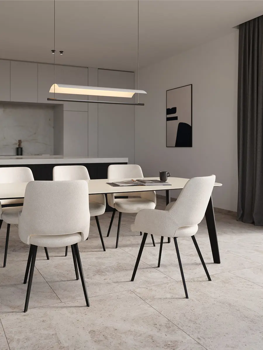 Minimalistische eetruimte met ovale eettafel, zes licht gestoffeerde stoelen en hanglamp, open keuken op de achtergrond.