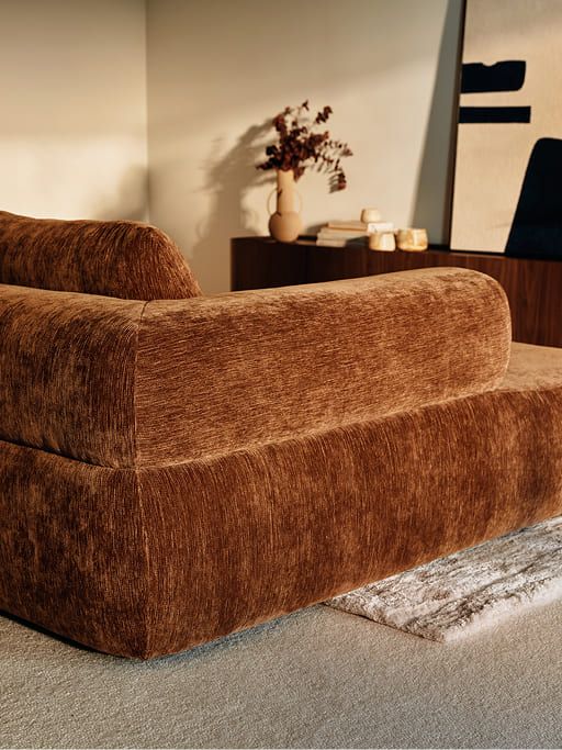 Bruine zetel met afgeronde vormen in een warm interieur met donkere kast en decoratieve accenten.