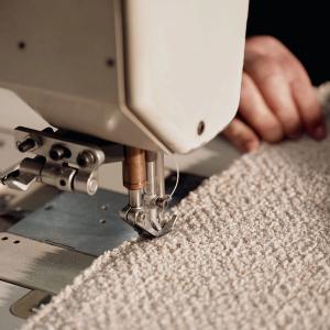Naaimachine stikt de beige bouclé-stof voor de Duomo-zetel, met handen die de stof geleiden.