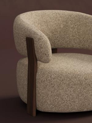 Close-up van een beige gestoffeerde fauteuil met gebogen rugleuning, ronde zitting en donker houten frame.