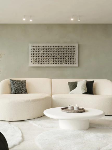 Table basse Artisano en forme de galet blanche devant un canapé beige dans un intérieur moderne et apaisant.