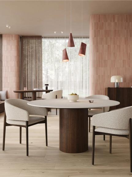 Ronde Amato eettafel met licht tafelblad en ronde houten poot, omringd door beige gestoffeerde stoelen in een warme eetkamer.