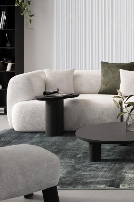Canapé Tortona clair avec des coussins sur un tapis vert, avec une table basse ronde noire et une table d'appoint avec un magazine et un vase avec des branches.