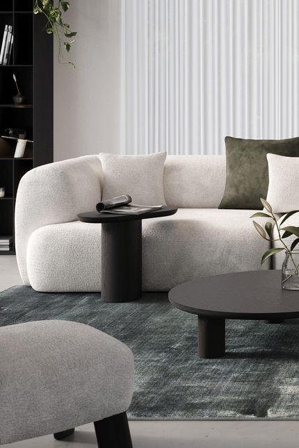 Canapé Tortona clair avec des coussins sur un tapis vert, avec une table basse ronde noire et une table d'appoint avec un magazine et un vase avec des branches.