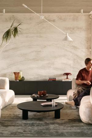 Luxe zithoek met zachte, ronde bank, zwarte salontafel en decoratieve objecten, een persoon zit comfortabel.