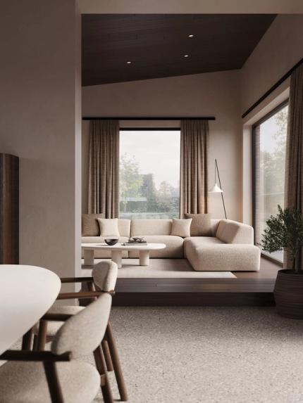 Doorkijk naar een zithoek met beige hoekzetel en lage ronde salontafel, naast een eetruimte met lichte stoelen en grote ramen.